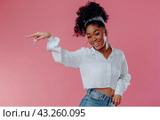 A photo of an excited woman in jeans and a rumpled shirt, standing full-length on a pink background and pointing her finger to the side. Стоковое AI-изображение, AI-художник Ярославский Максим / Фотобанк Лори