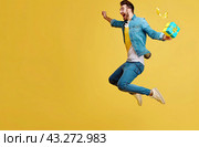 A happy young man with a gift box in his hand is jumping for joy on a yellow background. Copy space. Стоковое AI-изображение, AI-художник Ярославский Максим / Фотобанк Лори