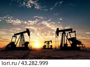 Scene of oil drilling derricks in desert at sunset, oilfield for fossil fuels output and crude oil production, evening. Image of drill rig and pump jack. Petroleum produced concept. Copy ad text space. Стоковое AI-изображение, AI-художник Aleksandr Golubev / Фотобанк Лори