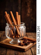 Ceylon cinnamon sticks in glass plate on wooden board, rustic style. Still life natural food of sri lankan cinnamon sticks on table at grey wall. Delicious tasty healthy concept. Copy ad text space. Стоковое AI-изображение, AI-художник Aleksandr Golubev / Фотобанк Лори