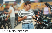 Interested young girl thoughtfully comparing bicycle models in shop, considering handlebar system, while picking perfect bike for fitness and travel. Стоковое видео, видеограф Яков Филимонов / Фотобанк Лори