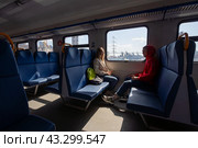 Пассажиры в современном региональном электропоезде. Люди едут в комфортное электричке. За окном видны корабли и православный собор. Поезд отправляется от железнодорожной станции Владивосток. Приморский край, Россия. Путешествие по Дальнему Востоку России. (2023 год). Редакционное фото, фотограф Андрей Степанов / Фотобанк Лори