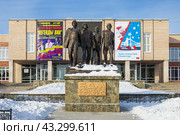 Памятник «БАМ — дорога дружбы», город Северобайкальск, Республика Бурятия, Сибирь, Россия. Памятник, посвящённые строителям Байкало-Амурской магистрали, около здания дворца культуры «Железнодорожник». На фасаде ДК афиша концерта «Легенды ВИА» и баннер с надписью «Ярких путешествий в Новом году!». (2024 год). Редакционное фото, фотограф Андрей Степанов / Фотобанк Лори