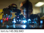 Curious boy exploring robotics and technology in a lab environment. Стоковое AI-изображение, AI-художник Антон Гвоздиков / Фотобанк Лори