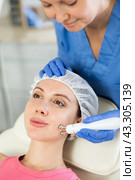 Adult woman cosmetologist doing microcurrent procedure to young woman. Стоковое фото, фотограф Яков Филимонов / Фотобанк Лори