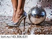 Women's legs in luxurious shiny pumps with heels at a party or disco on the background of a silver mirrored disco ball. The queen of the dance floor. Стоковое AI-изображение, AI-художник Photojuli / Фотобанк Лори
