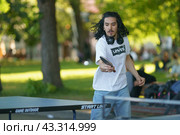 Moscow, Russia - June 4, 2021: Sports activity in the public park. Young man plays table tennis, healthy lifestyle theme. Leisure concept. Ping-pong game in hot sunny day. Редакционное фото, фотограф YuryKara / Фотобанк Лори