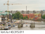 Kaliningrad, Russia - June 20, 2022: Cityscape in day. Bank of Pregol River and the Fishing village. Famous touristic location. New buildings. Yubileyny bridge. Construction crane. New buildings. Редакционное фото, фотограф YuryKara / Фотобанк Лори
