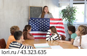 Group of curious preteen learners and young female teacher with flag of USA in classroom of academy. Стоковое видео, видеограф Яков Филимонов / Фотобанк Лори