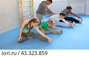 Family in gym during group sports training under guidance of trainer performs stretching on floor. Стоковое видео, видеограф Яков Филимонов / Фотобанк Лори