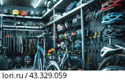Interior of a bicycle accessories and equipment store. There is a bicycle in the center of the frame, and in the background are racks with a variety of bicycle helmets of different colors and models. Bicycle saddles and other accessories, including pumps and bicycle maintenance tools, hang on the walls. The room is brightly lit, creating a modern and professional atmosphere. The image perfectly conveys the range of products and their organization in the store, which makes it attractive to customers. Стоковое AI-изображение, AI-художник Анна Кривицкая / Фотобанк Лори