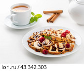Belgian waffles with raspberries, banana, chocolate syrup. Breakfast with tea on white background. Стоковое фото, фотограф Natalia Gdovskaia / Фотобанк Лори