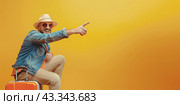 A happy male tourist sits on a suitcase and points his finger in front of him. Copy space. Стоковое AI-изображение, AI-художник Ярославский Максим / Фотобанк Лори