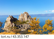 Lake Baikal in autumn. The famous Shamanka rock framed by yellowed larches on a sunny October morning. Traveling around the autumn island of Olkhon. Picturesque landscape. Natural background. Стоковое фото, фотограф Виктория Катьянова / Фотобанк Лори