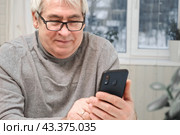 Hoary old man looking at web camera, holding phone, talking with children, wife online. Senior grandpa smiling chatting with friends, family via video call. Modern technologies and older generation. Стоковое фото, фотограф Марина Демидюк / Фотобанк Лори