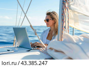 A woman is leisurely using a laptop on a sailboat in the midst of the ocean under the azure sky. Стоковое AI-изображение, AI-художник Юрий Поздников / Фотобанк Лори
