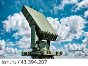Modern air defence radar of military mobile missile launcher system of green color at blue cloudy sky background. Air defense installation outdoors. Concept of modern army industry. Copy ad text space. Стоковое AI-изображение, AI-художник Aleksandr Golubev / Фотобанк Лори