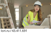 Female foreman in a protective helmet and a yellow vest checks the execution of repair work using a laptop. Стоковое видео, видеограф Яков Филимонов / Фотобанк Лори