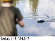 A 5-year-old boy in a yellow panama hat launches a radio-controlled boat in a pond. Children's fun and street games. Child's leisure time. Стоковое фото, фотограф Photojuli / Фотобанк Лори