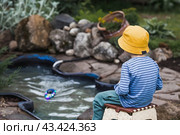 A 5-year-old boy in a yellow panama hat launches a radio-controlled boat in a pond. Children's fun and street games. Child's leisure time. Стоковое фото, фотограф Photojuli / Фотобанк Лори
