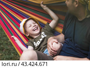 Summer holidays for children in the fresh air. A cute little boy with his father is having fun on a hammock in the backyard. A child and a dad in a hammock. Стоковое фото, фотограф Photojuli / Фотобанк Лори