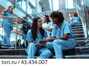 A group of medical university students communicate sitting on the stairs during a break between classes. Стоковое AI-изображение, AI-художник Ярославский Максим / Фотобанк Лори