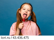 Portrait of happy cheerful little girl lick chupa-chups candy enjoy sweet snack wear good look clothes isolated over blue color background. Стоковое фото, фотограф Ирина Михайличенко / Фотобанк Лори