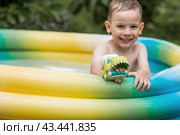 It's a hot day. A cute boy is swimming and splashing in the pool. A happy little boy smiles at the camera. Splashes of water are flying in all directions. The concept of summer holidays with children. Стоковое фото, фотограф Photojuli / Фотобанк Лори