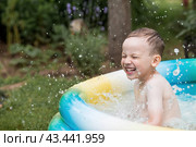 It's a hot day. A cute boy is swimming and splashing in the pool. A happy little boy smiles at the camera. Splashes of water are flying in all directions. The concept of summer holidays with children. Стоковое фото, фотограф Photojuli / Фотобанк Лори