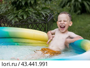 It's a hot day. A cute boy is swimming and splashing in the pool. A happy little boy smiles at the camera. Splashes of water are flying in all directions. The concept of summer holidays with children. Стоковое фото, фотограф Photojuli / Фотобанк Лори
