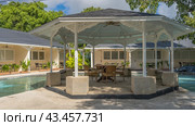 Gazebo in the recreation area by the swimming pool. A table and wicker chairs under a canopy. Around the perimeter there are villas with green vegetation on open terraces. Philippines. Стоковое фото, фотограф Вера Ивановна Кубарева / Фотобанк Лори