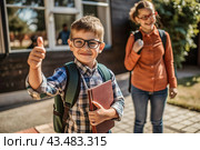A boy with glasses shows the class with his hand. The child goes to school for the first time. A child with a school bag and a book. A child in the classroom on the background of a blackboard. Back to school. Стоковое AI-изображение, AI-художник Photojuli / Фотобанк Лори