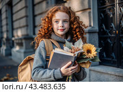 A pretty red-haired girl with glasses and a bouquet of autumn flowers goes to school for the first time. A child with a school bag, a book and flowers. A child on a city street. Back to school. Стоковое AI-изображение, AI-художник Photojuli / Фотобанк Лори