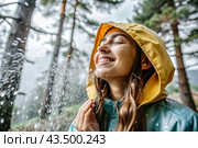 Close-up. A happy young woman in a raincoat enjoys the rain on the background of a green forest, the concept of enjoying a natural leisurely life, environment, lifestyle. Стоковое AI-изображение, AI-художник Photojuli / Фотобанк Лори