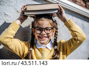 A pretty girl with glasses and books on her head. The child goes to school for the first time. A child in the fresh air. Back to school. Стоковое AI-изображение, AI-художник Photojuli / Фотобанк Лори