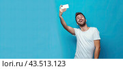A handsome man in a white T-shirt on a blue background takes a selfie, sending greetings via an online call. Стоковое AI-изображение, AI-художник Ярославский Максим / Фотобанк Лори