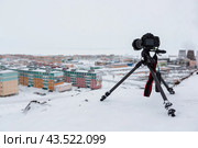 A digital camera on a tripod photographs a snow-covered northern city in the Arctic. Tourism and winter photography in the Far North. Cold snowy weather. Travel photography equipment. Photo hobby. Стоковое фото, фотограф Андрей Степанов / Фотобанк Лори