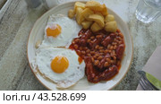 Plate with traditional English breakfast of fried eggs with French fries and white beans stewed in tomato sauce with chorizo sausages. Стоковое видео, видеограф Яков Филимонов / Фотобанк Лори
