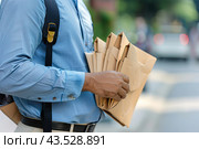 An unidentified courier holds a bundle of letters for delivery against the backdrop of an urban landscape. The concept of a courier service. Стоковое AI-изображение, AI-художник Ярославский Максим / Фотобанк Лори