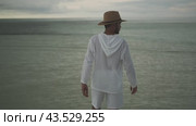 A young man in light white clothes and a hat walks barefoot in the rain on the water of the sea. Stormy evening clouds are in the background. Maldives. Стоковое видео, видеограф Aleksey Kidisyuk / Фотобанк Лори