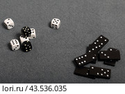 White dice with black markings. They lie on a surface covered with a coarse gray cloth. Among them are two black dice with white markings. Next door are dominoes. Стоковое фото, фотограф Vadzim Yakubovich / Фотобанк Лори