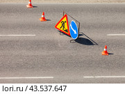 Road signs on an asphalt road: temporary warning sign Road works, sign, obstacle avoidance on the right and red striped traffic cones on a sunny summer day. Road repair and improvement concept. Стоковое фото, фотограф Виктория Катьянова / Фотобанк Лори
