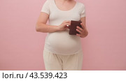 Pregnant woman holding an empty wallet without money in her hand, studio pink background. Стоковое видео, видеограф Андрей Журавлев / Фотобанк Лори
