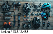 A set of cycling accessories and equipment laid out on a wooden surface. In the center of the composition are various bicycle helmets: black and blue. Around them are other items such as sunglasses, bicycle saddles, gloves, pedals, cycling shoes, headphones, bottle cages and other accessories. The image is made in muted colors, creating an atmosphere of order and professionalism. Стоковое AI-изображение, AI-художник Анна Кривицкая / Фотобанк Лори
