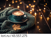 A seasonal drink. Delicious hot cappuccino in a mug with a saucer and a knitted snood, a scarf on a wooden table in the interior of the cafe. It's a rainy autumn day. Стоковое AI-изображение, AI-художник Photojuli / Фотобанк Лори