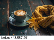 A seasonal drink. Delicious hot cappuccino in a mug with a saucer and a knitted snood, a scarf on a wooden table in the interior of the cafe. It's a rainy autumn day. Стоковое AI-изображение, AI-художник Photojuli / Фотобанк Лори