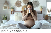 On a bed, a woman who is pregnant is sitting and using a tissue to wipe her nose. Стоковое AI-изображение, AI-художник Юрий Поздников / Фотобанк Лори