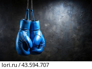 Professional blue boxing gloves hang on a black background with a space to copy. Стоковое AI-изображение, AI-художник Photojuli / Фотобанк Лори