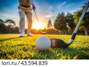 The banner. A white ball and a metal golf club are lying on the lawn in the hands of a man against the sunset background. An advertisement for a golf game at a country club. Free space for text. Стоковое AI-изображение, AI-художник Photojuli / Фотобанк Лори