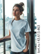 Woman in white blank t-shirt leaning on railing, looking out window. Generative AI. Стоковое AI-изображение, AI-художник Александра Селина / Фотобанк Лори